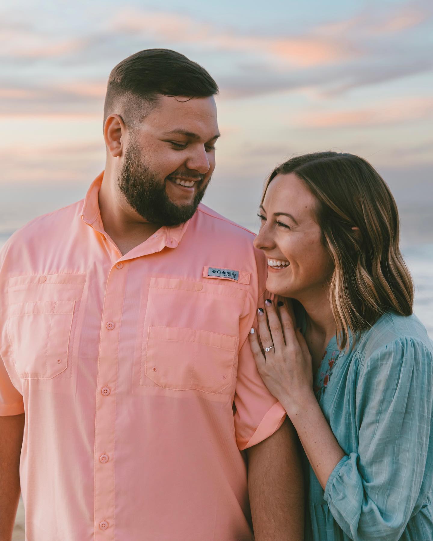 Newly engaged couple smile at beach.