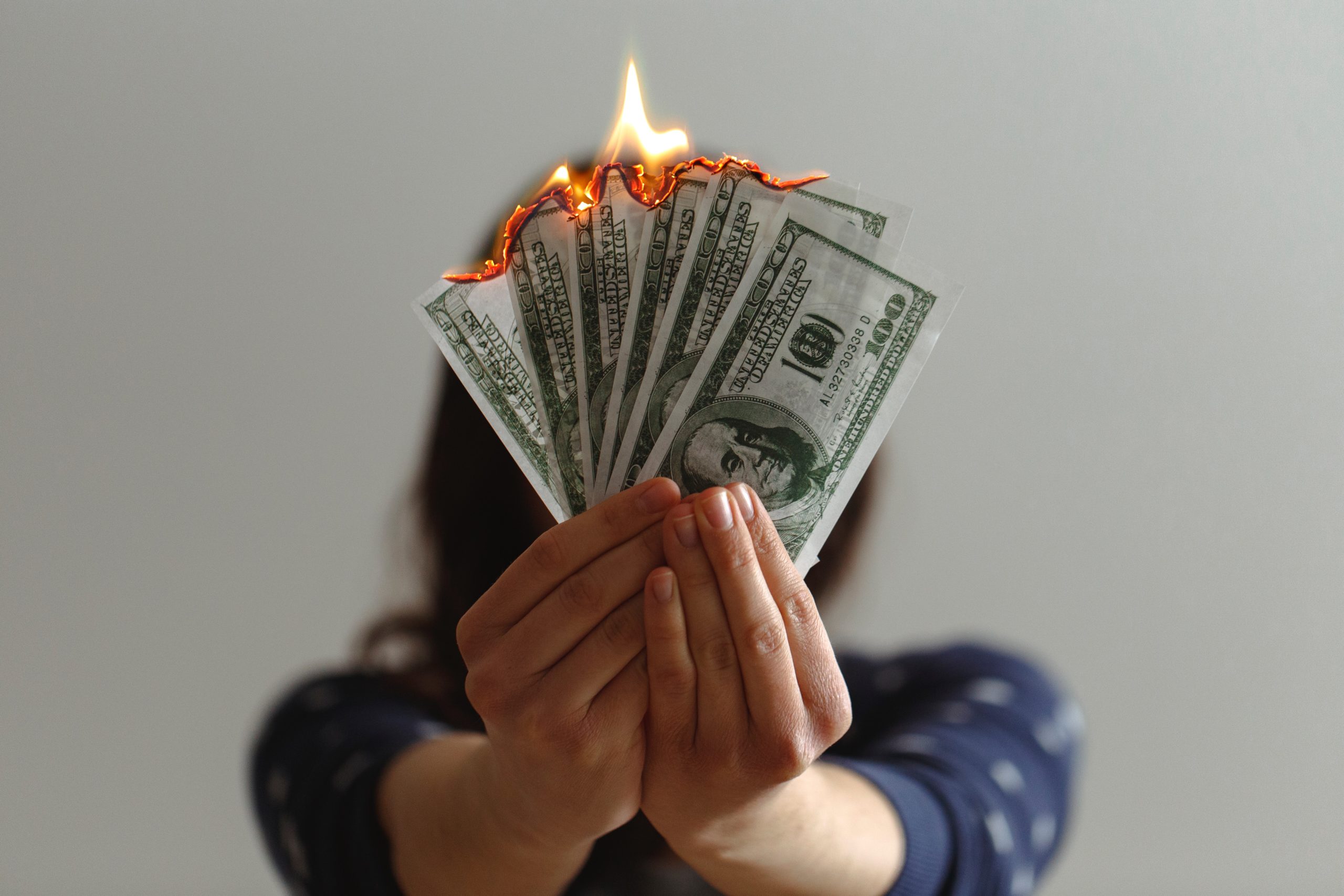 A woman's hands hold a fan made of $100 bills that is on fire.