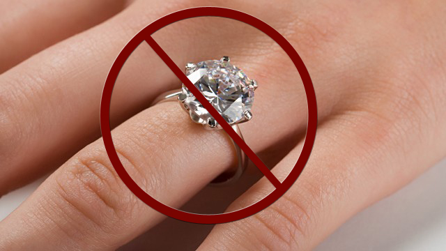 A large diamond ring on a finger with a red cirlce and line going through it over the image.